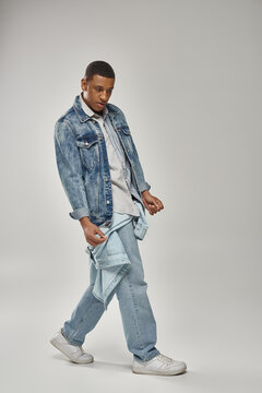 young trendy african american man in stylish denim outfit posing on white backdrop, fashion
