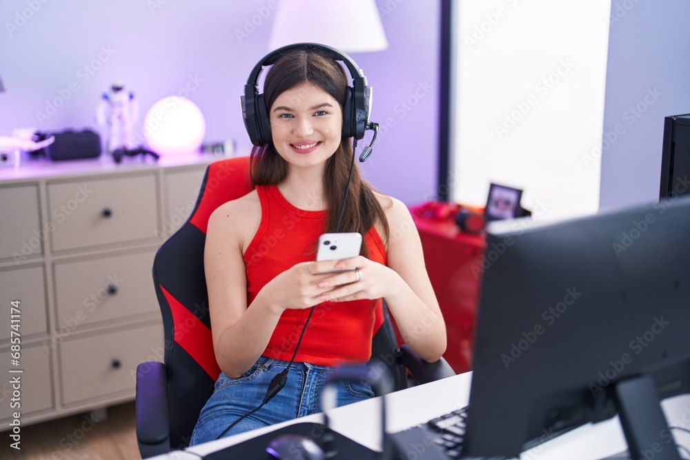 Wall mural Young caucasian woman streamer using computer and smartphone at gaming room