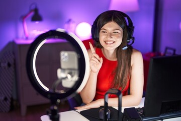 Young caucasian woman playing video games recording with smartphone smiling happy pointing with hand and finger to the side