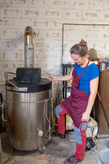 A smiling woman checking a ceramic kiln in her workshop.
