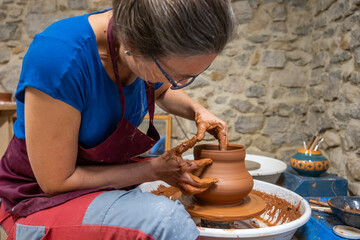 A woman heightening a piece of ceramic on the wheel.