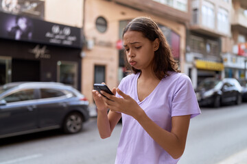 Young african american woman using smartphone with worried expression at street