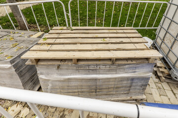 A pallet of paving stones for paving a street in the middle of white metal fences