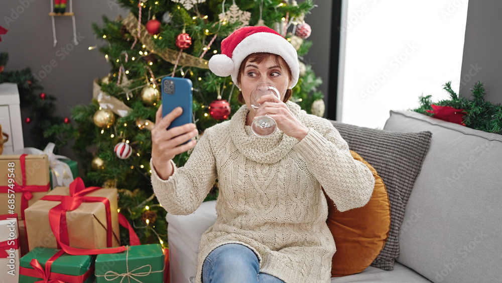 Wall mural Mature hispanic woman doing video call drinking wine at home