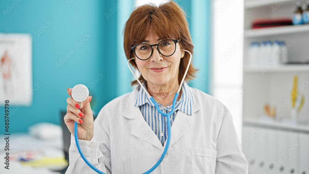 Wall mural Middle age woman doctor smiling confident holding stethoscope at clinic