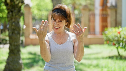 Middle age woman smiling confident doing coming gesture with hand at park