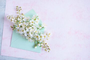 Bouquet of bird cherry flowers and white fruit flowers in an envelope on white-pink decorative paper and space for text. Greeting card for the holiday.