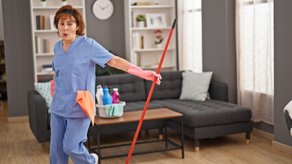 Middle age woman professional cleaner cleaning and dancing home