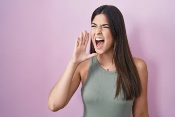 Fotobehang Hispanic woman standing over pink background shouting and screaming loud to side with hand on mouth. communication concept. © Krakenimages.com