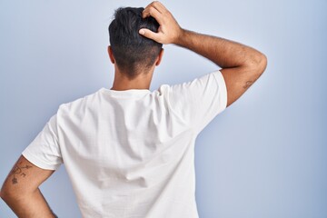 Hispanic man standing over blue background backwards thinking about doubt with hand on head