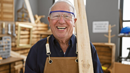 Confident senior man, a professional carpenter, smiling while securely holding a wood plank in...