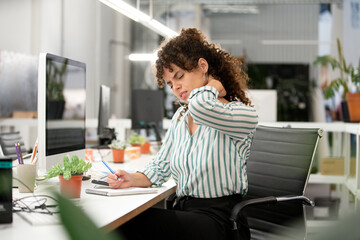 Stressed woman suffering from a neck contracture while sitting in office - obrazy, fototapety, plakaty