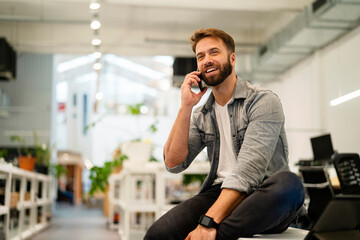 Male entrepreneur talking on smart phone while sitting on table