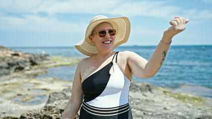 Middle age grey-haired woman tourist wearing swimsuit and summer hat doing come gesture at the beach