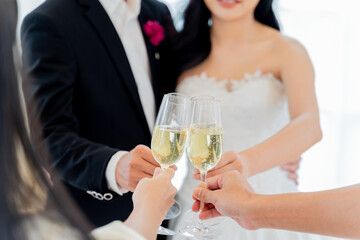 Close-up of bridal toast with champagne, a joyful cheer at wedding reception among friends. Asian bride and groom cheers and toasts with friends