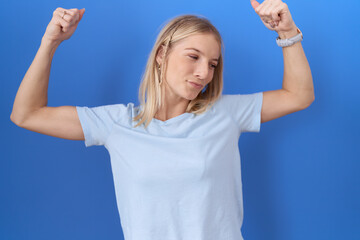 Obraz premium Young caucasian woman wearing casual blue t shirt showing arms muscles smiling proud. fitness concept.