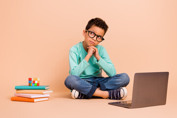 Full body photo of little minded boy sit floor look empty space contemplate laptop book rubik cube...