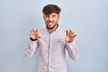 Arab man with beard standing over blue background smiling funny doing claw gesture as cat,...