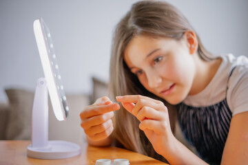 Young woman trying to apply contact lenses in front of mirror. Young girl trying on new contact lenses. Close up of girl trying on beauty medical contact lenses