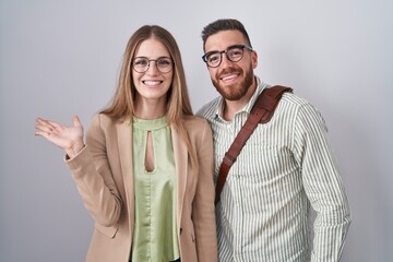 Young couple standing over white background smiling cheerful presenting and pointing with palm of hand looking at the camera.