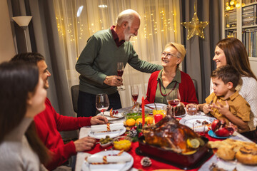 Grandfather is making a toast at the table. Family celebrating Christmas together eating homemade food.