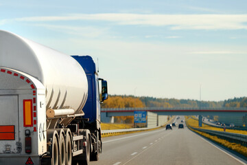 Dangerous goods transportation by semi truck with propane tank. The tank truck has a side view and shows hazard labels for high-temperature liquid and miscellaneous hazards. The truck follows the ADR - obrazy, fototapety, plakaty