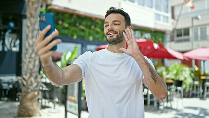 Fototapeta na wymiar Young hispanic man smiling confident having video call at coffee shop terrace
