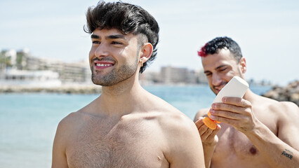 Two men tourist couple applying sunscreen lotion at beach