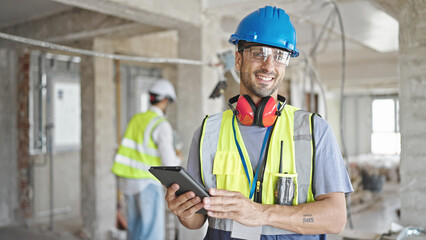 Two men builders smiling confident using touchpad at construction site