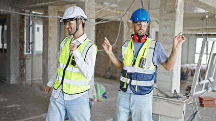 Two men builders smiling confident dancing at construction site