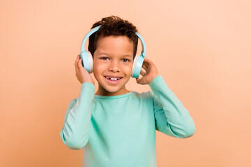 Photo of cute charming boy wear trendy clothes listen music modern technology isolated on beige color background