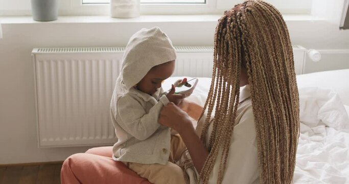 crying naughty little girl using smartphone doesn not want to put on clothes, wants to watch cartoon, slow motion, mom buttons her kids sweater, family going for a walk, outside, street