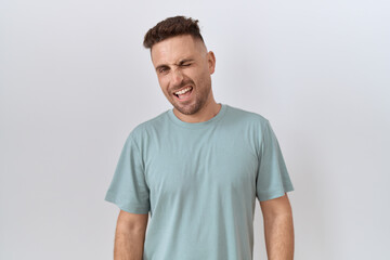 Hispanic man with beard standing over white background winking looking at the camera with sexy expression, cheerful and happy face.