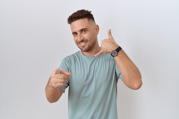 Fototapeta premium Hispanic man with beard standing over white background smiling doing talking on the telephone gesture and pointing to you. call me.