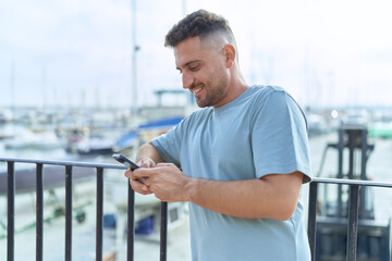 Young hispanic man smiling confident using smartphone at seaside