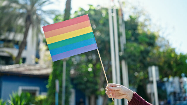 Young hispanic man holding rainbow flag at street