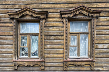 Ancient facade of a wooden house with two windows. Typical Russian wooden architecture.