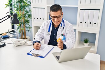 Young latin man doctor writing on document holding pills at clinic