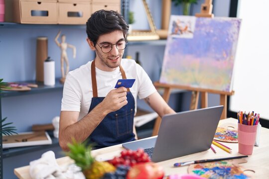 Young hispanic man artist using laptop and credit card at art studio