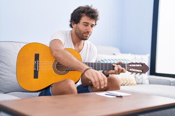 Young hispanic man playing classical guitar composing song at home