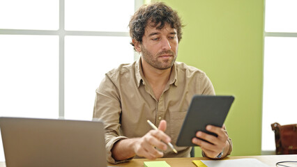 Young hispanic man business worker using touchpad writing notes at office