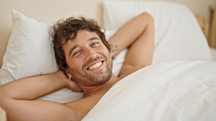 Fototapeta na wymiar Young hispanic man relaxed on bed smiling shirtless at bedroom