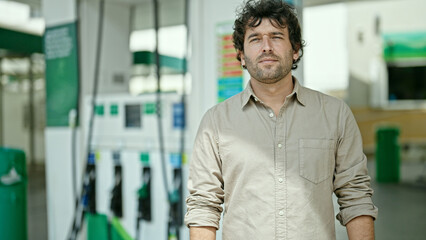 Young hispanic man standing with serious expression at petrol station