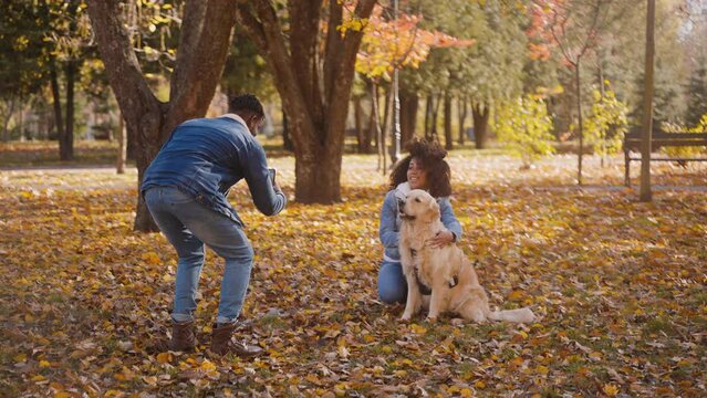Black woman hugs Labrador posing for photo done by man on phone