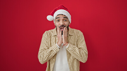 Young hispanic man surprise expression wearing christmas hat over isolated red background