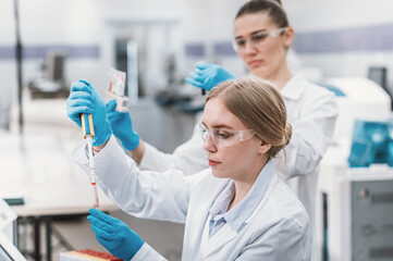 team of laboratory technicians conduct series of tests on  chemical analyzer in laboratory. Two female scientists work in modern equipped computer laboratory doing tests with tubes and pipette