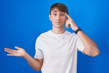 Caucasian blond man standing over blue background confused and annoyed with open palm showing copy...