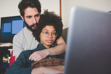 young multiethnic couple indoor using computer sitting couch