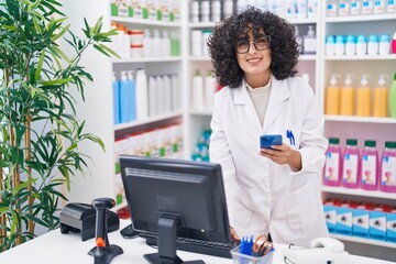 Young middle eastern woman pharmacist using smartphone and computer at pharmacy