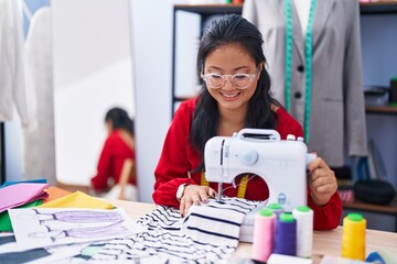 Young chinese woman tailor smiling confident using sewing machine at atelier